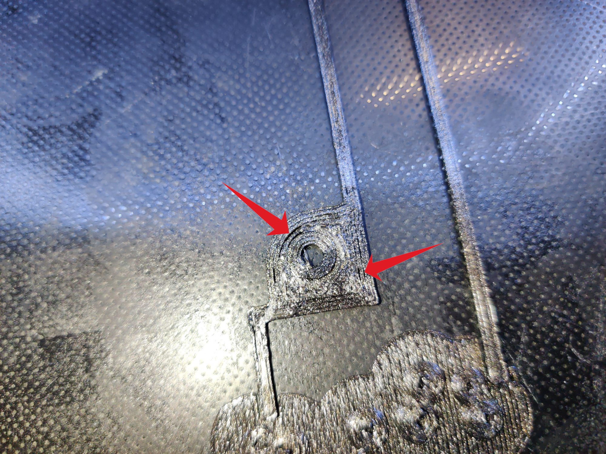 Close-up of a 3D printed part on the build plate currently in progress of being printed. Two arrows point at locations where the perimeter lines aren't attached to each other.