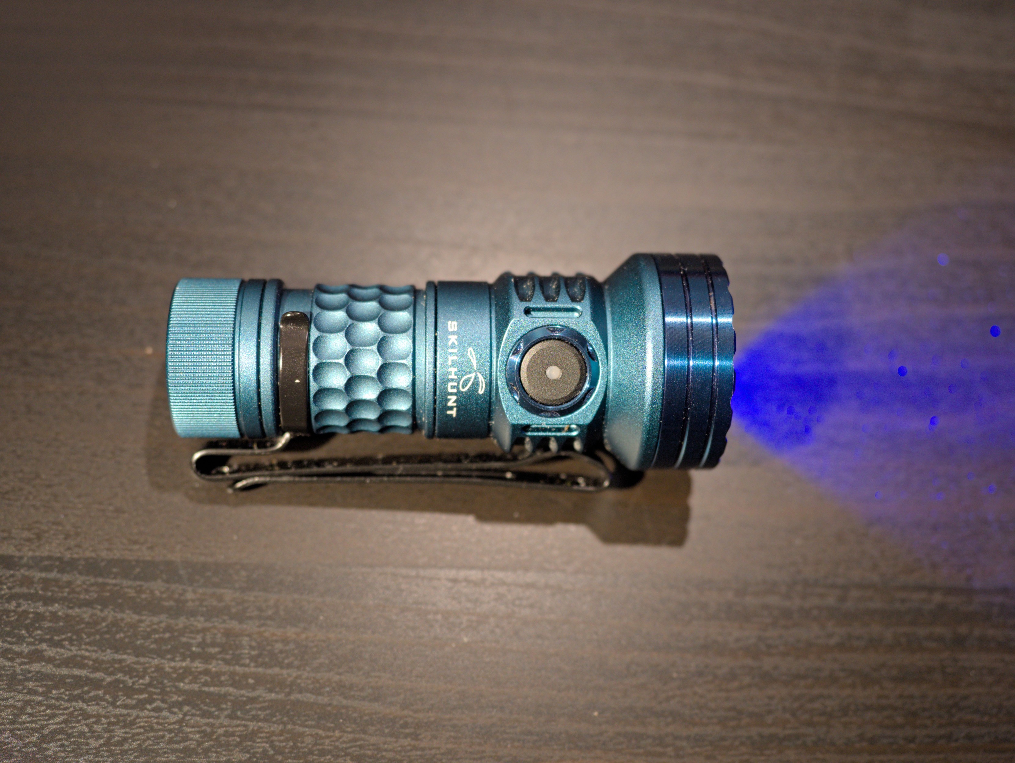 A blue Skilhunt MiX-7 flashlight emitting blue light